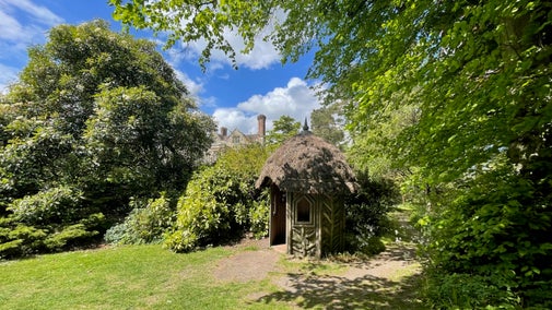 Glimpse of a manor house above a thatched garden summer house